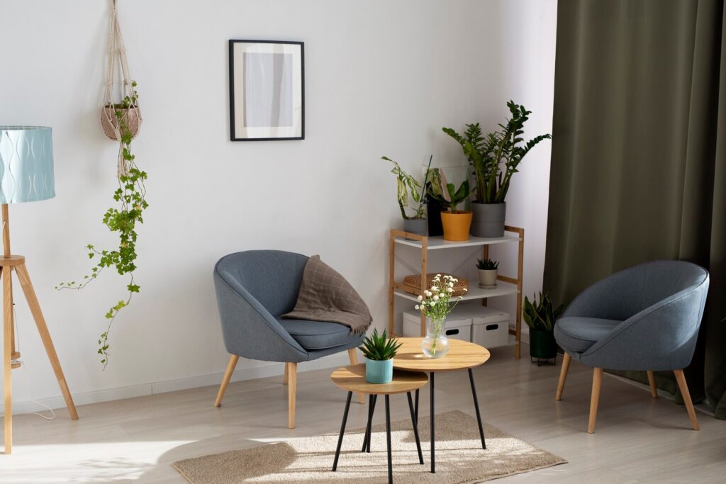 Cozy living space featuring two blue armchairs, a wooden coffee table, plants, a decorative lamp, and a wall art piece.