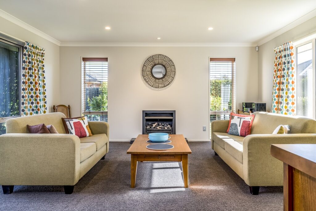 Bright living room with two cozy sofas, a wooden coffee table, and large windows adorned with colorful curtains.