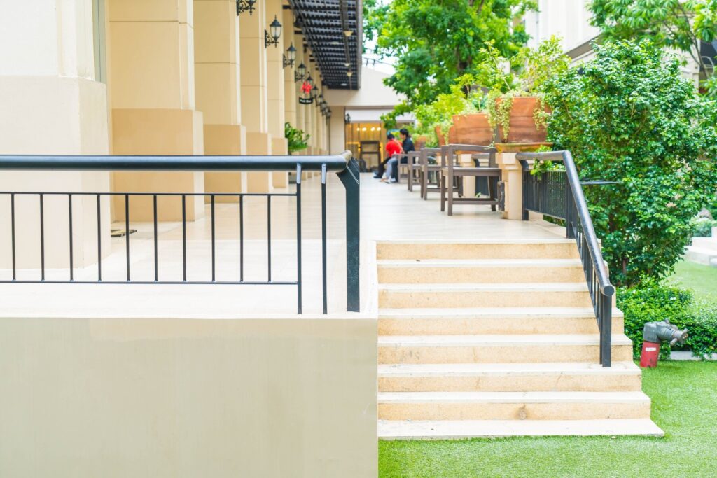A serene walkway with steps leading down, flanked by greenery and outdoor seating, creating a welcoming atmosphere.