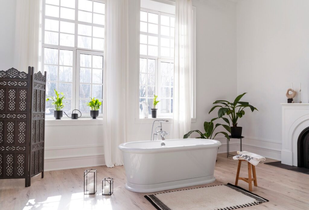 Bright, airy bathroom featuring a freestanding bathtub, large windows with plants, a wooden stool, and decorative lanterns.