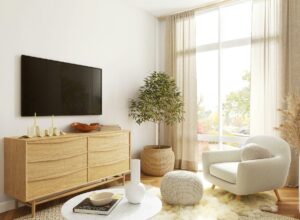 Cozy living room featuring an oak sideboard, a white plush armchair, a large window, potted plants, and soft textiles for a warm ambiance.