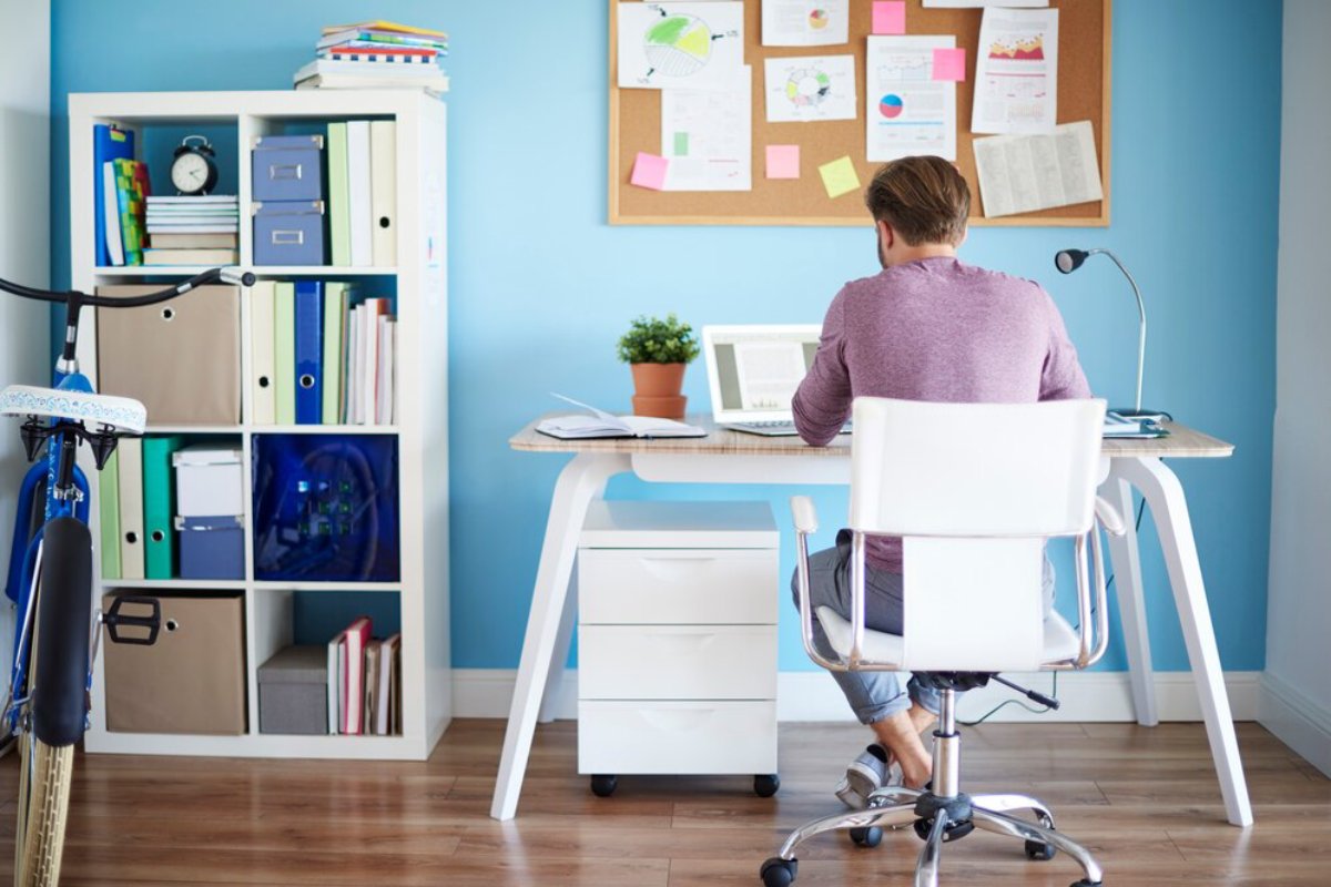 A man working at a modern desk in a bright office, with a bike, bookshelves, and a bulletin board in the background.