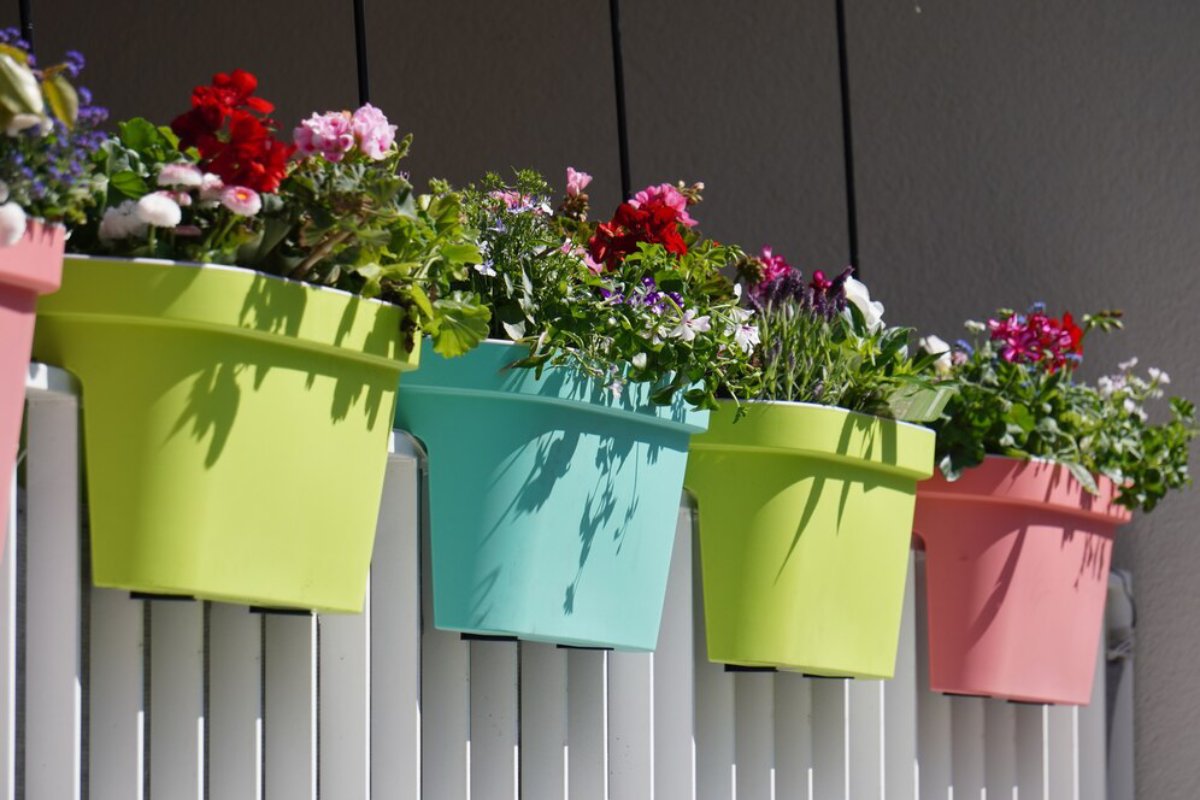Colorful flower pots filled with blooming plants hang on a white fence, creating a vibrant and cheerful outdoor display.